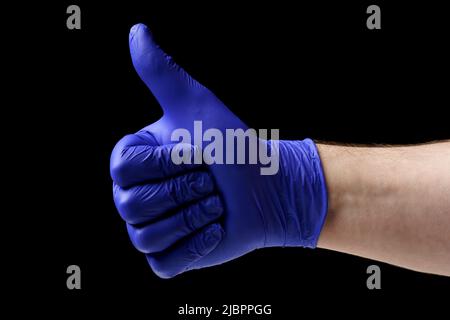 Man showing thumbs up. Close-up of a male hand in a blue latex glove on a black background. Stock Photo