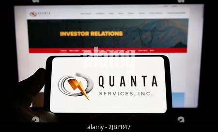 Person holding cellphone with logo of American infrastructure company Quanta Services Inc. on screen in front of webpage. Focus on phone display. Stock Photo