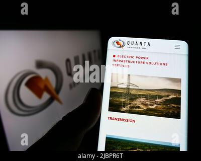 Person holding cellphone with webpage of US infrastructure company Quanta Services Inc. on screen with logo. Focus on center of phone display. Stock Photo