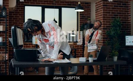 Goofy creepy zombie trying to photocopy her own head in office. Brain-eating dead walking couple with deep and bloody wounds acting bizarre and spooky while trying to act as humans. Stock Photo