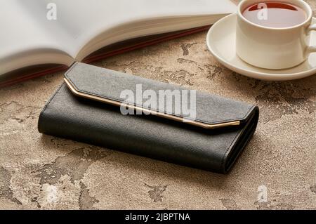 A black woman's purse lies on a concrete background with a cup of coffee and a book Stock Photo