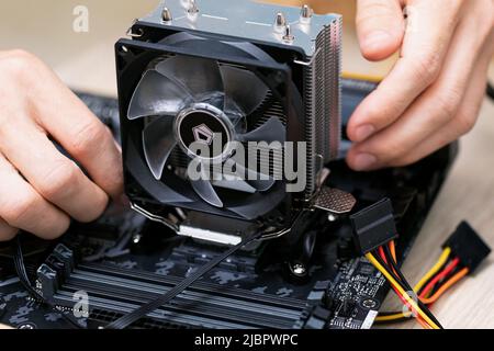 Technician man installs aluminum air-cooled heatsink on desktop CPU covered with heatsink paste. Air Cooler CPU. PC assembly and modernization Stock Photo