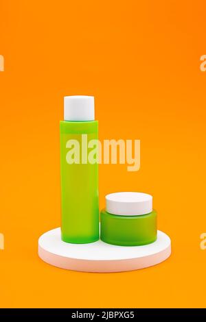 Set of green cosmetic bottle and jar on white podium against orange background. Summer collection skin care product. Stock Photo