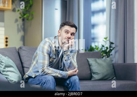 Sad and pensive man sitting on the couch at home Stock Photo