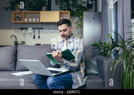 A man studying at home online uses a laptop, sitting on the couch smiling Stock Photo