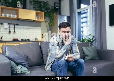 A sick man at home sitting on the couch has a cold cough and runny nose Stock Photo