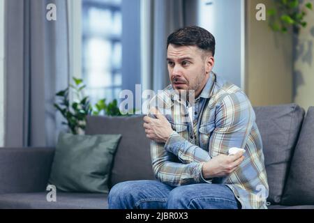 A sick man at home sitting on the couch has a cold cough and runny nose Stock Photo