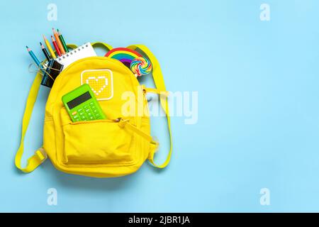 Back to school, education concept Yellow backpack with school supplies - notebook, pens, eraser rainbow, numbers isolated on blue background Top view Stock Photo