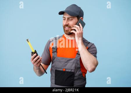 Man builder in uniform talk on mobile phone and holding a tape measure. Studio shoot Stock Photo