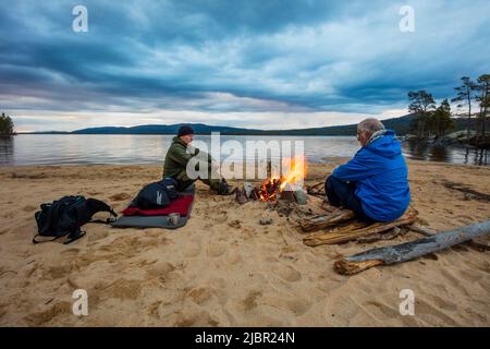 Two canoe paddlers and a dog by a bonfire on a cloudy summer evening by the lake Isteren, Engerdal kommune, Innlandet fylke, Norway, Scandinavia. Stock Photo