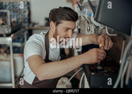 Smiling young worker repairing coffee machine in a workshop Stock Photo