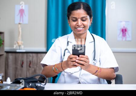 happy smiling women doctor busy using mobile phone at clinic - concept of technology, surfing web and vitural health consultation Stock Photo