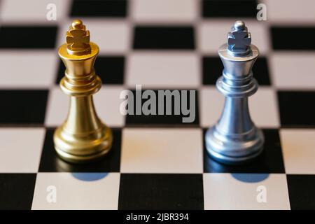 Close up shot of golden and silver chess kings placed against each other on chessboard Stock Photo