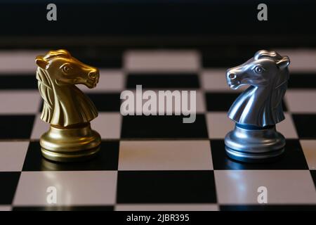 Closeup golden and silver horse knights places against each other on chessboard against gray background Stock Photo