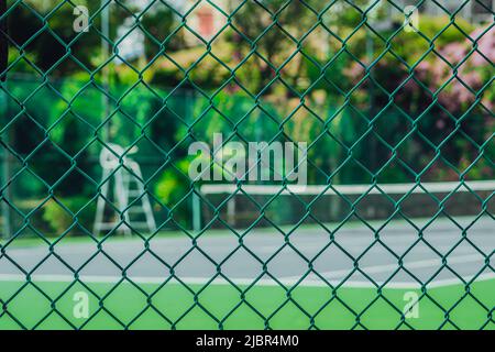 Empty tennis court in modern fashion hotel, tower for referee, view through metal net fence. Bright fresh tropical green colours. Sport fun summer Stock Photo