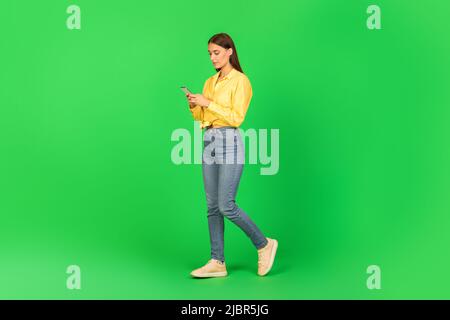 Woman Using Mobile Phone Browsing Internet Walking Over Green Background Stock Photo