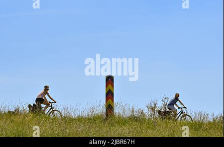 03 June 2022, Brandenburg, Reitwein: Cyclists are on the Oder-Neisse Cycle Path, which is located in the Oderbruch on the dike on the German-Polish border river Oder. The Oder-Neisse Cycle Path is a long-distance cycle path in the Czech Republic and Germany that is about 630 kilometers long. It largely follows Germany's eastern border with Poland. The Oder-Neisse Cycle Route runs in a south-north direction for about 55 kilometers through the Czech Republic, starting at the source of the Neisse River and following it to where the Neisse flows into the Oder. Westward of the Oder, the trail then Stock Photo