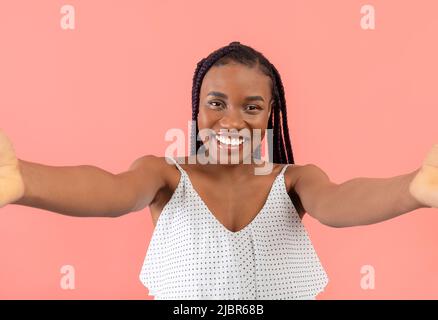 Smiling young black woman taking selfie with smartphone, chatting online on pink studio background Stock Photo