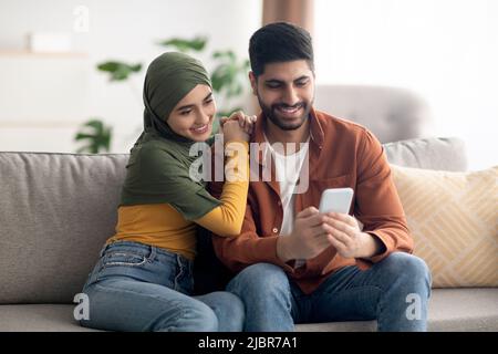 Cheerful Muslim Couple Using Smartphone Together At Home Stock Photo