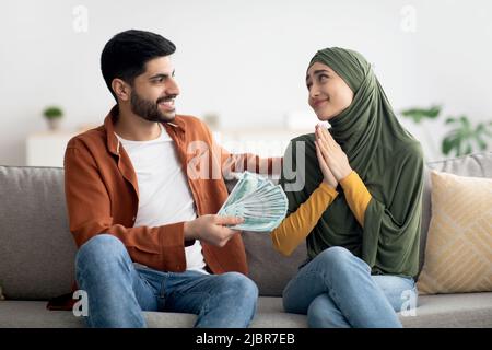 Muslim Husband Giving Money To Thankful Wife Sitting At Home Stock Photo