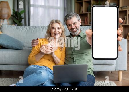 Great App. Middle Aged Spouses Demonstrating Blank Smartphone With White Screen Stock Photo
