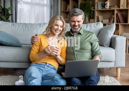 Happy Middle Aged Couple Spending Time With Laptop At Home Stock Photo