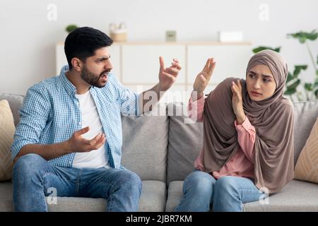 Aggressive Muslim Husband Shouting At Scared Wife Sitting At Home Stock Photo