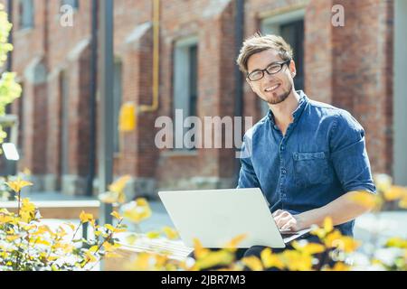 Young businessman with glasses near the office working on a laptop Stock Photo