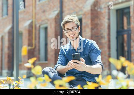 Young businessman outside the office sitting on a bench enjoying the phone smiling and happy Stock Photo