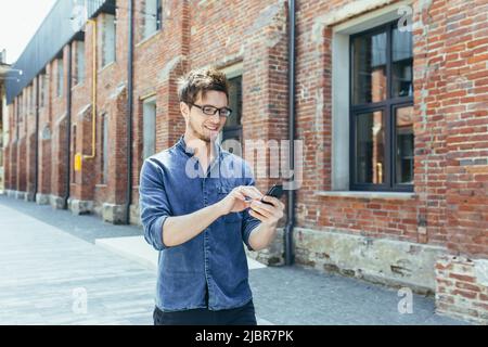 Young businessman uses phone outside office, happy and smiling man with smartphone Stock Photo