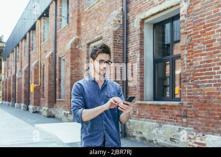 Young businessman uses phone outside office, happy and smiling man with smartphone Stock Photo