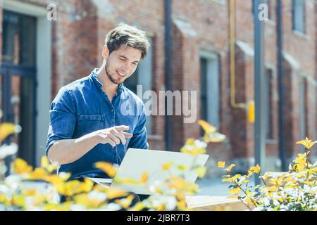 A young man with a beard uses a laptop for a video call, a cold man smiles and talks to friends remotely looking at a computer screen Stock Photo