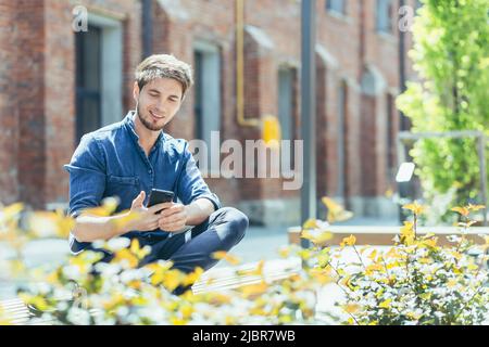 Young man outside student campus, student enjoys phone smiling Stock Photo