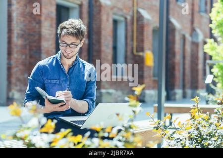 Young student on campus studying and working online on laptop, man in casual clothes outside office Stock Photo