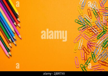 Colored pencils and stationery multi-colored paper clips on a orange background Stock Photo