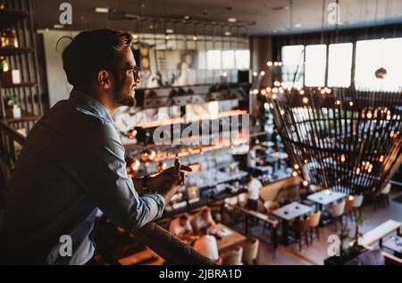 Happy businessman, restaurant owner proudly looking at crowded restaurant Stock Photo