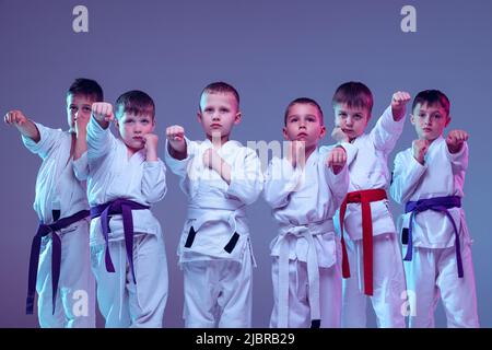 Group of kids, different boys, taekwondo athletes in white doboks in action isolated on lilac color background. Concept of sport, martial arts Stock Photo