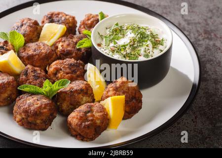 Juicy Baked Greek Meatballs Keftedakia with tzatziki sauce and lemon on a white plate on a table. Horizontal Stock Photo