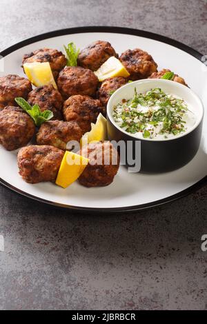 Keftedakia fried greek meatballs with tzatziki sauce and lemon on a white plate on a table. Vertical Stock Photo