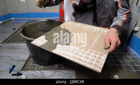 Applying mortar to tiles, close-up. The master of laying tiles, takes a mixture for gluing finishing materials to the wall, close-up. Handyman install Stock Photo