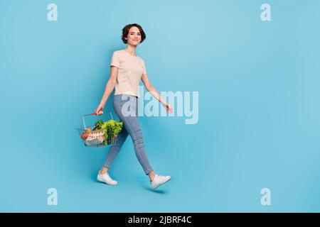 Full size photo of young lovely woman go shopping visit grocery store buy fresh greens isolated on blue color background Stock Photo
