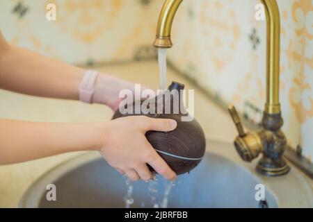 Woman washing aroma diffuser in faucet. Aromatherapy Concept. Wooden Electric Ultrasonic Essential Oil Aroma Diffuser and Humidifier. Ultrasonic aroma Stock Photo