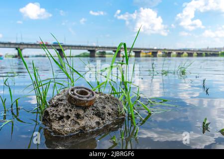 A river stone in the water on which lies a rusty metal bearing that pollutes the environment Stock Photo