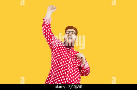 Funny happy crazy fat man standing on yellow background, raising his fist up and shouting YES Stock Photo