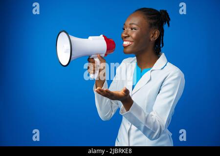 Afro american female doctor in white medical gown scream in megaphone in studio Stock Photo