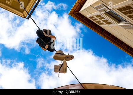 Old sneakers thrown over a telephone wire hanging down in urban environment as a symbol of commemorating a rite of passage or a way to bully someone. Stock Photo