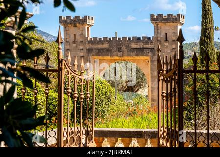 View through a rusty iron fence door over a stone handrail in front of a garden with vernal vegetation to the impressive arab castle style entrance. Stock Photo