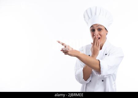 Woman chef looking at camera in surprise,  pointing  with finger  isolated on white background with copy space . Stock Photo