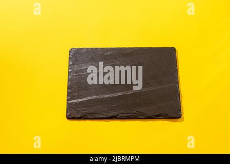 Front view of empty slate black stone plate on the yellow background Stock Photo