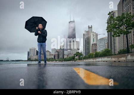 Rainy and windy day in city. Man with umbrella walking against Chicago cityscape. Stock Photo